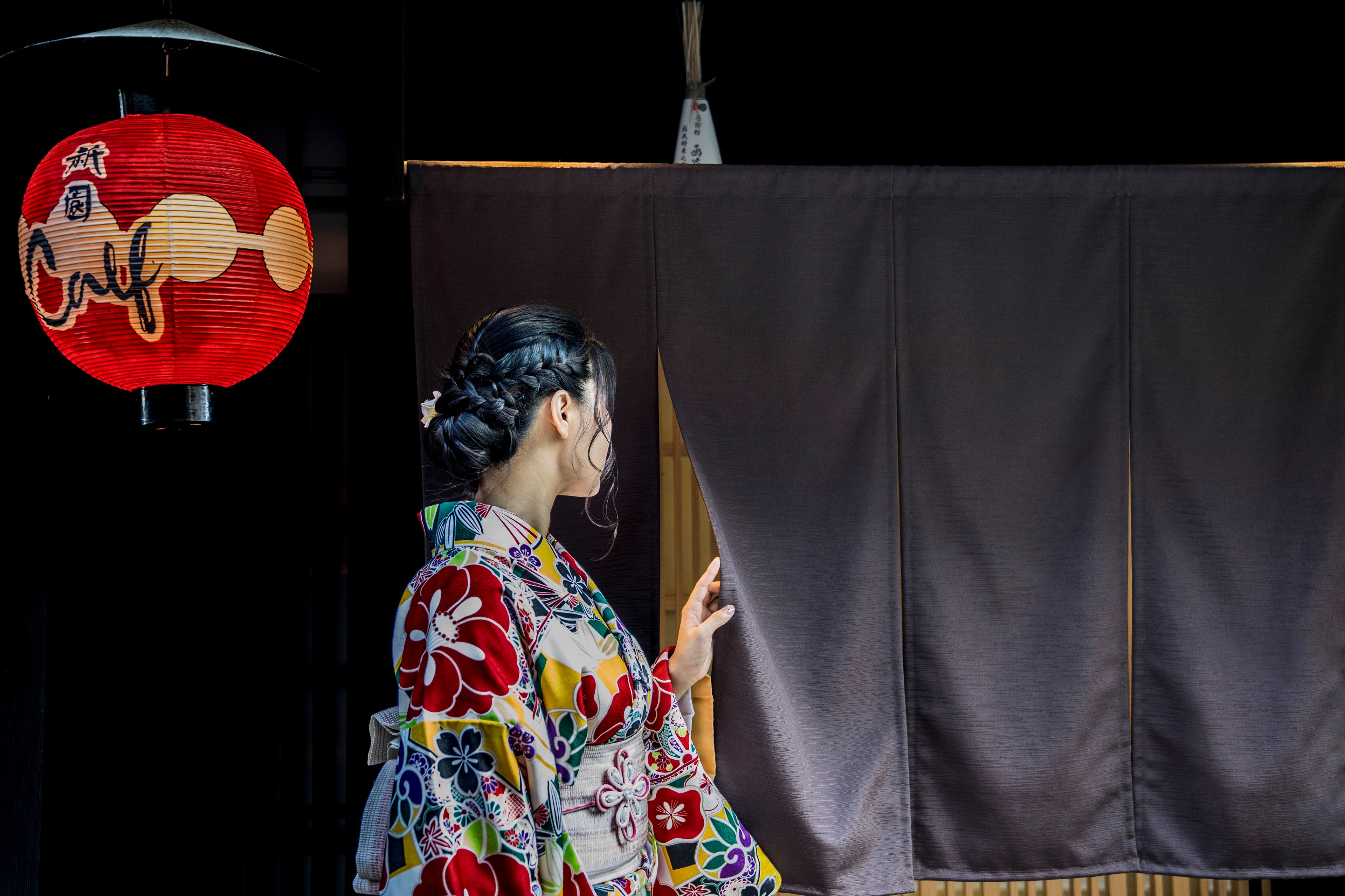 Woman in traditional Japanese kimono standing beside a noren curtain under a red lantern